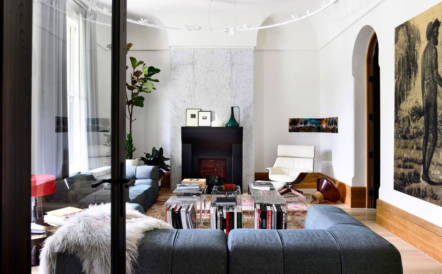 Salón con sofás azules, butaca en blanco, mesitas transparentes para libros, chimenea negra recubierta de mármol