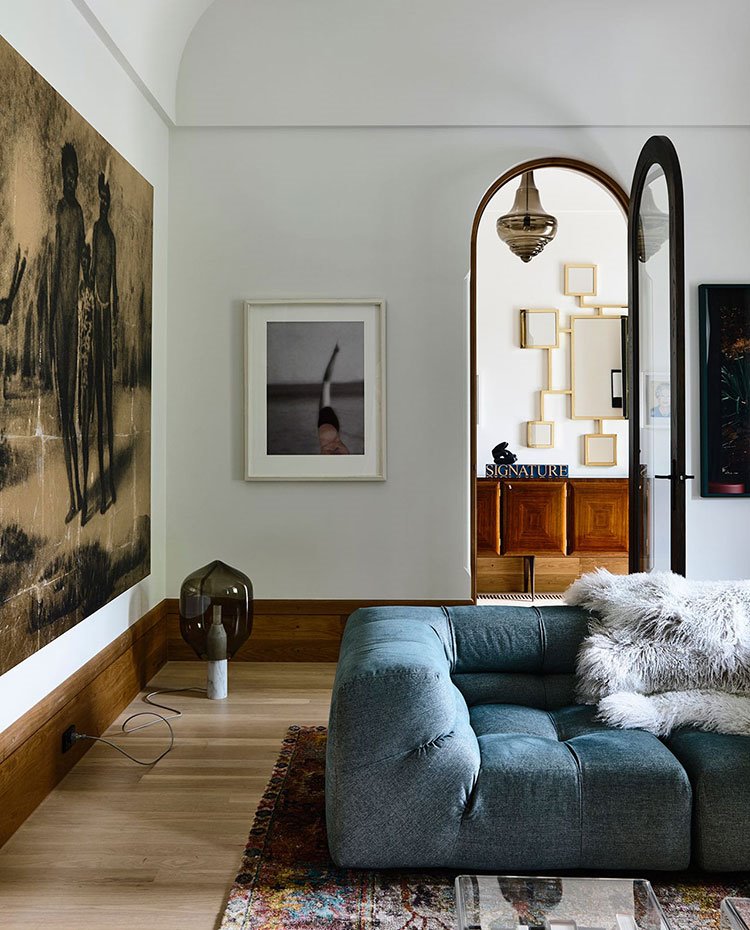 Salón junto a recibidor con puerta arqueada, sofá azul, alfombra de colores y manta de pelos gris
