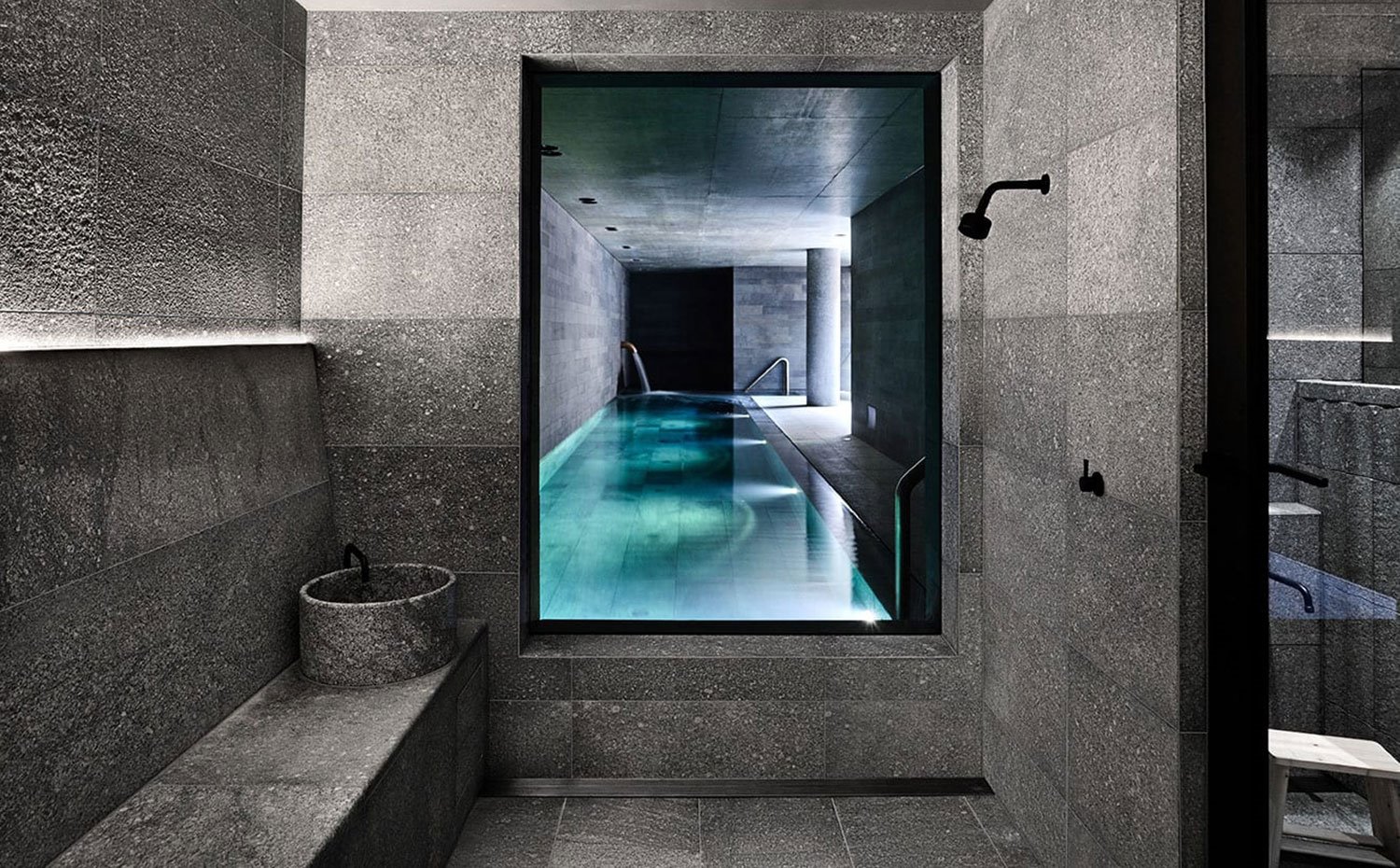 Zona de baño junto a piscina, con revestimiento de piedra gris y grifería en acabado negro