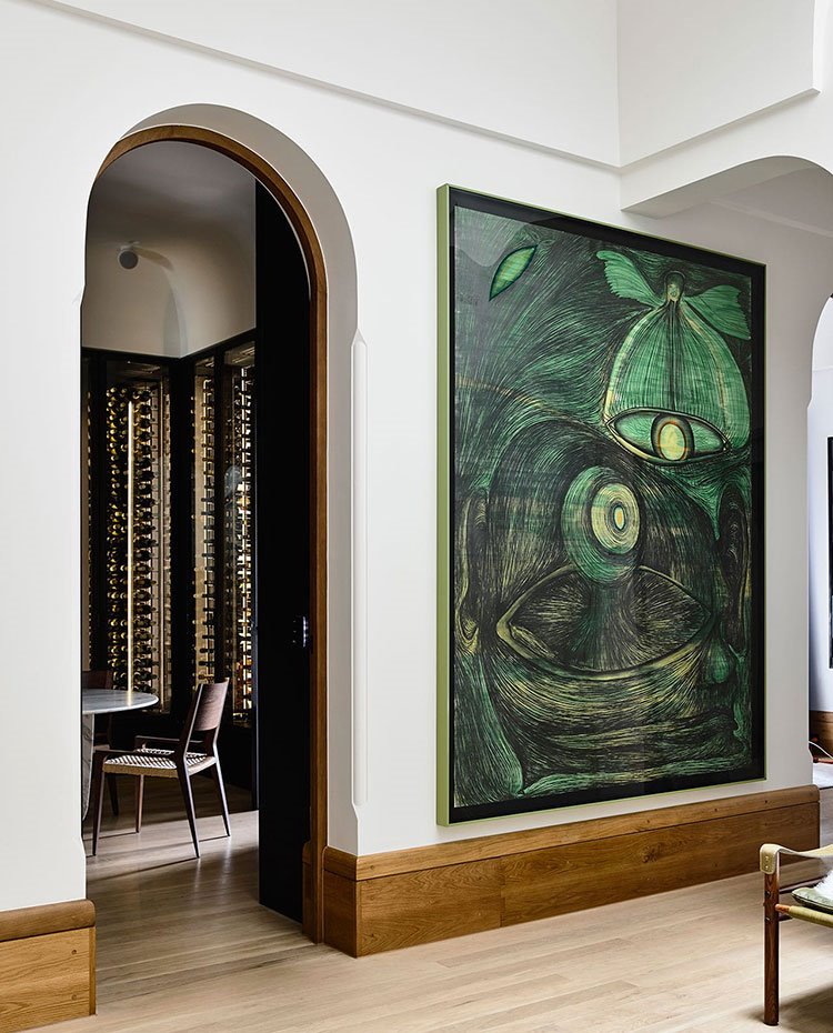 Zona de paso con gran pintura en tonos verdes, apertura arqueada hacia vinoteca