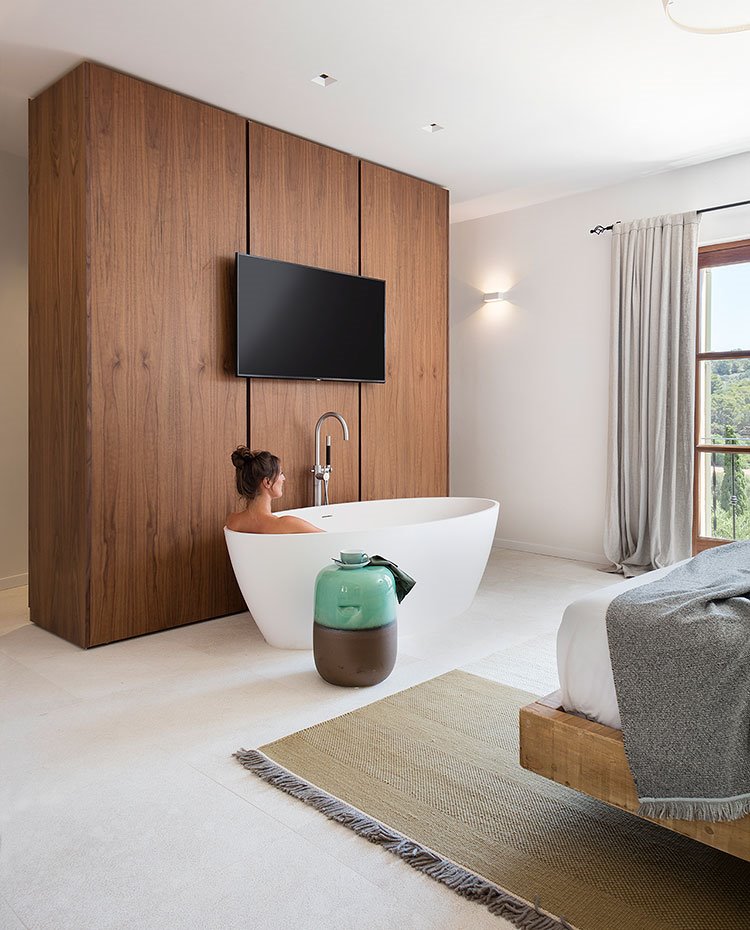 Bañera exenta dentro de dormitorio, frente a televisor, y mueble de madera