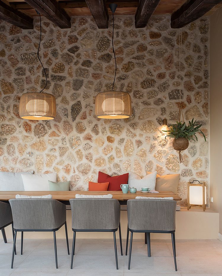 Comedor exterior con mesa de madera, sillas grises y banco de obra con cojines de colores