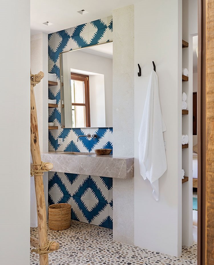 Encimera de lavamanos en piedra gris, revestimiento blanco y azul, estantes ocultos en hueco frontal