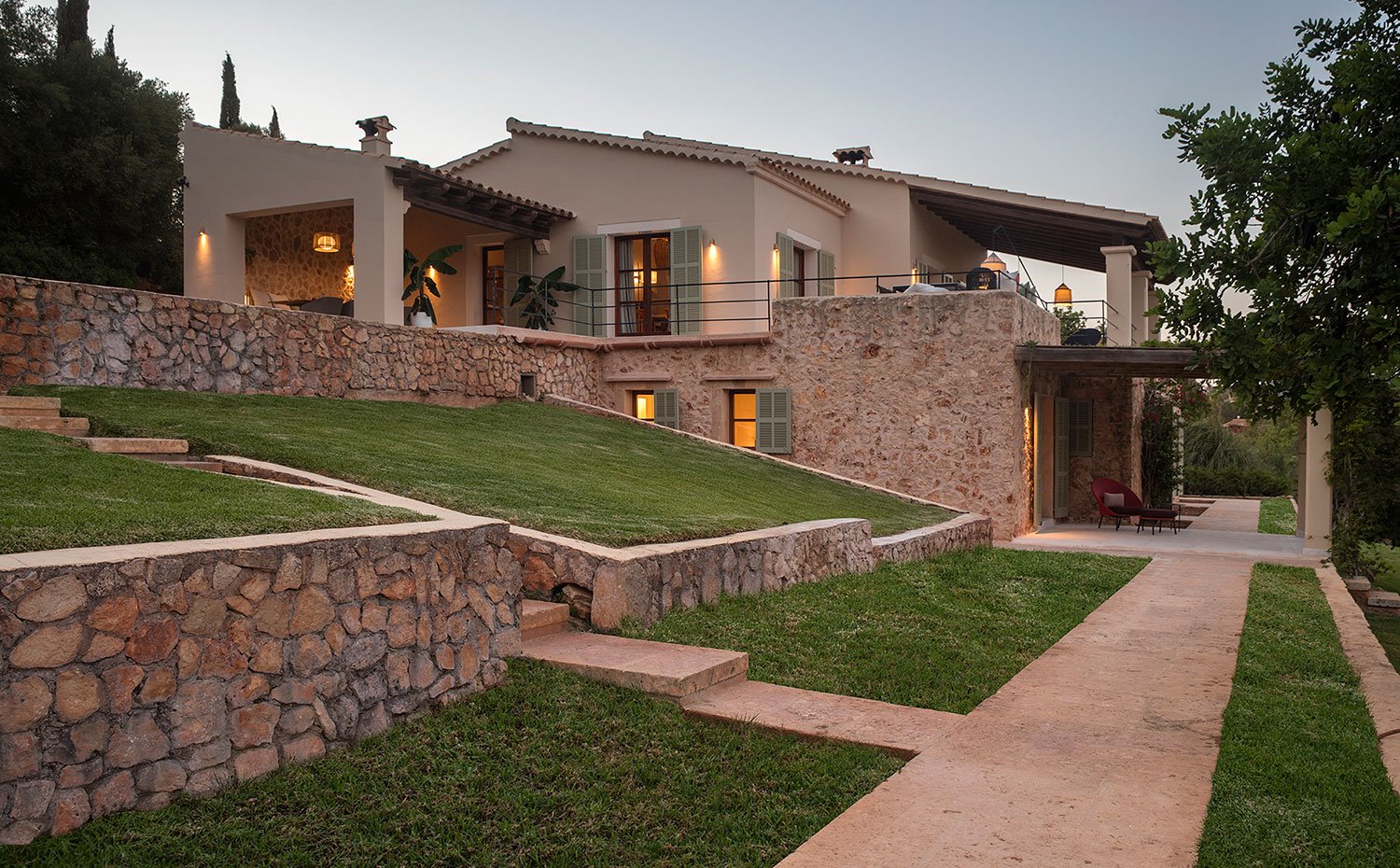 Exterior vivienda de piedra vista y beige, con zonas ajardinadas