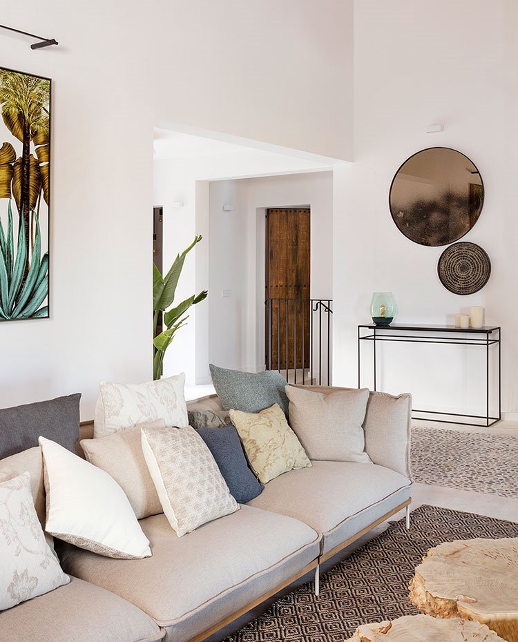 Salón con sofá beige y cojines en tonos tierra, alfombra en crudo y negro , mueble de acero negro