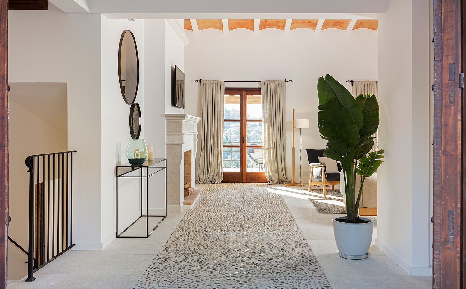 Zona de paso a salón, chimenea blanca, vuelta catalana en techo, perfilería de madera, cortinas de lino