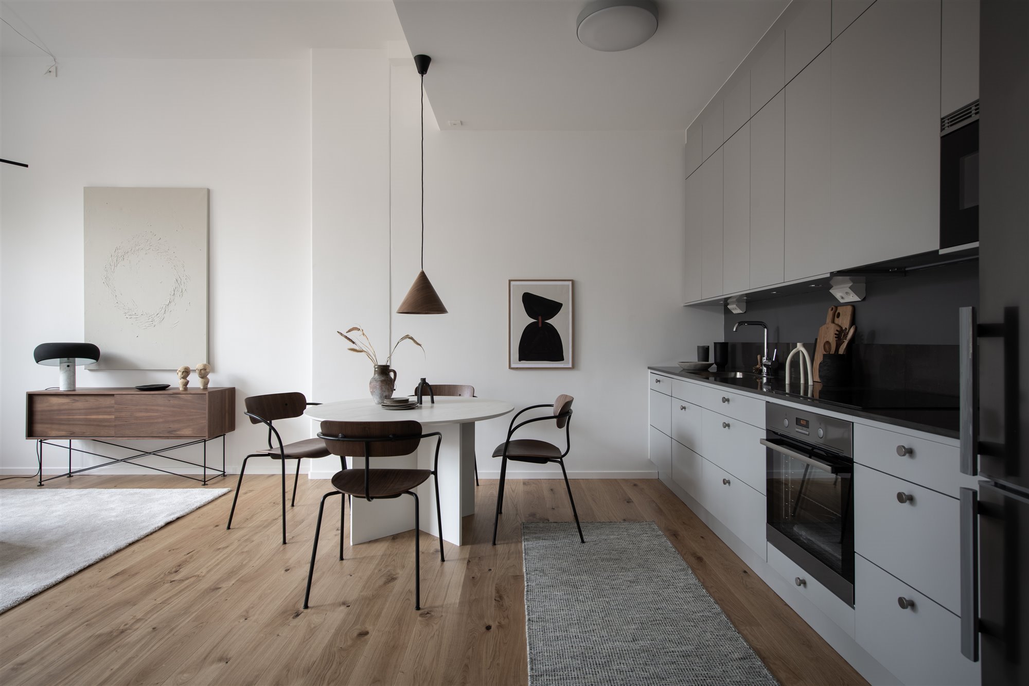 Cocina abierta, mesa de comedor circular blanca, sillas en marrón, consola madera a salón