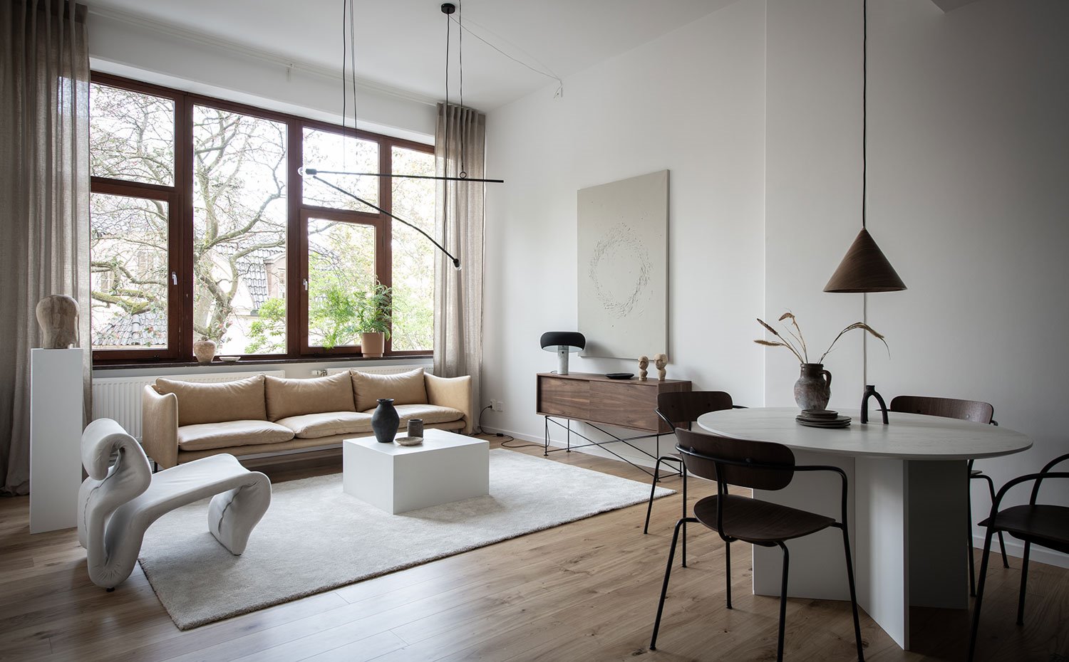 Comedor y salón con butaca cruda, sofá beige, mesa de centro blanca, luminaria suspendida negra