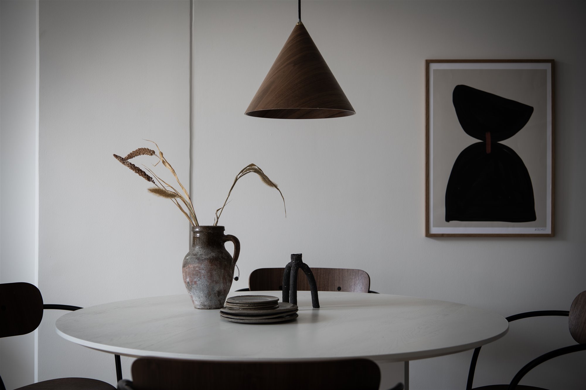 Mesa de comedor circular blanca, jarrón marrón, platos marrón, luminarias suspendida con pantalla cónica 