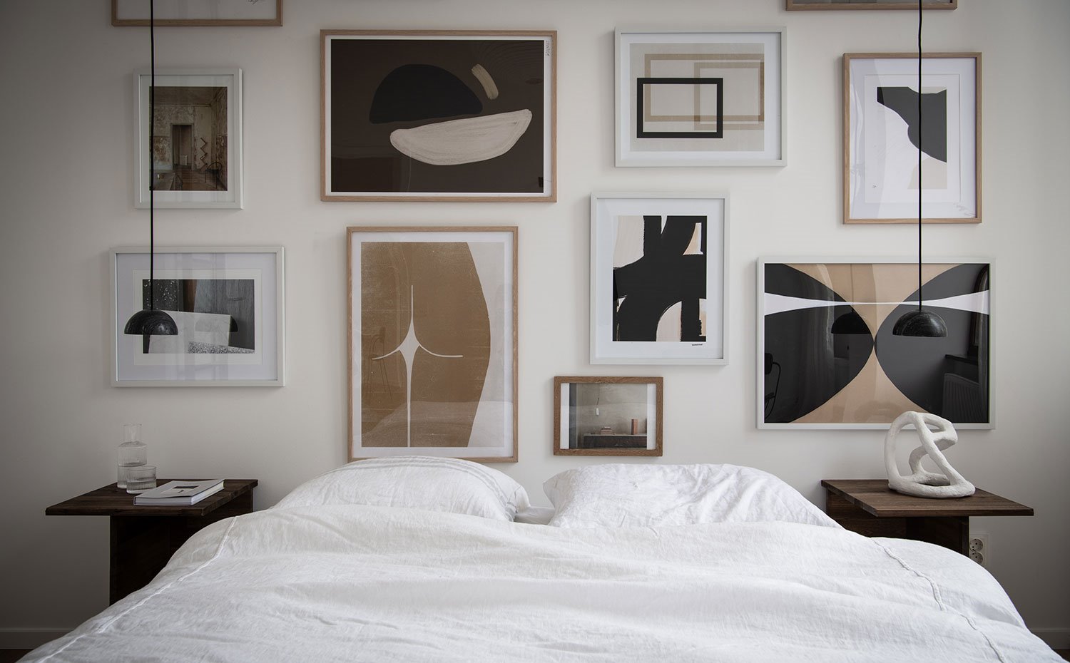 Mesillas de madera y luminarias suspendidas a gran altura junto a cama con lencería de color blanco