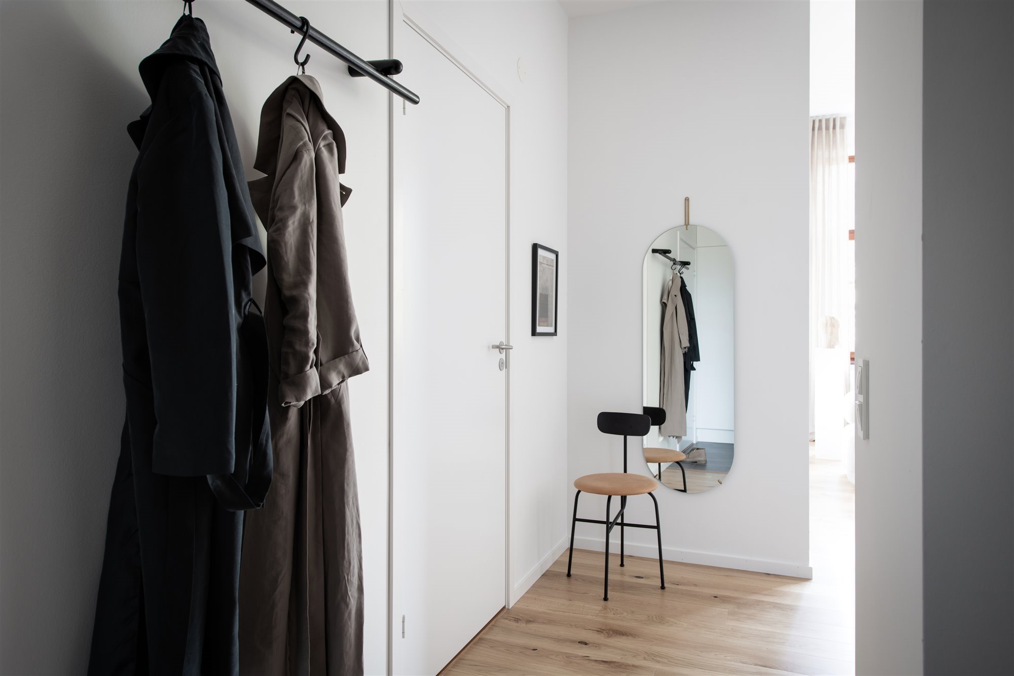 Puerta de acceso a vivienda, silla y espajo a pared, riel negro para colgador