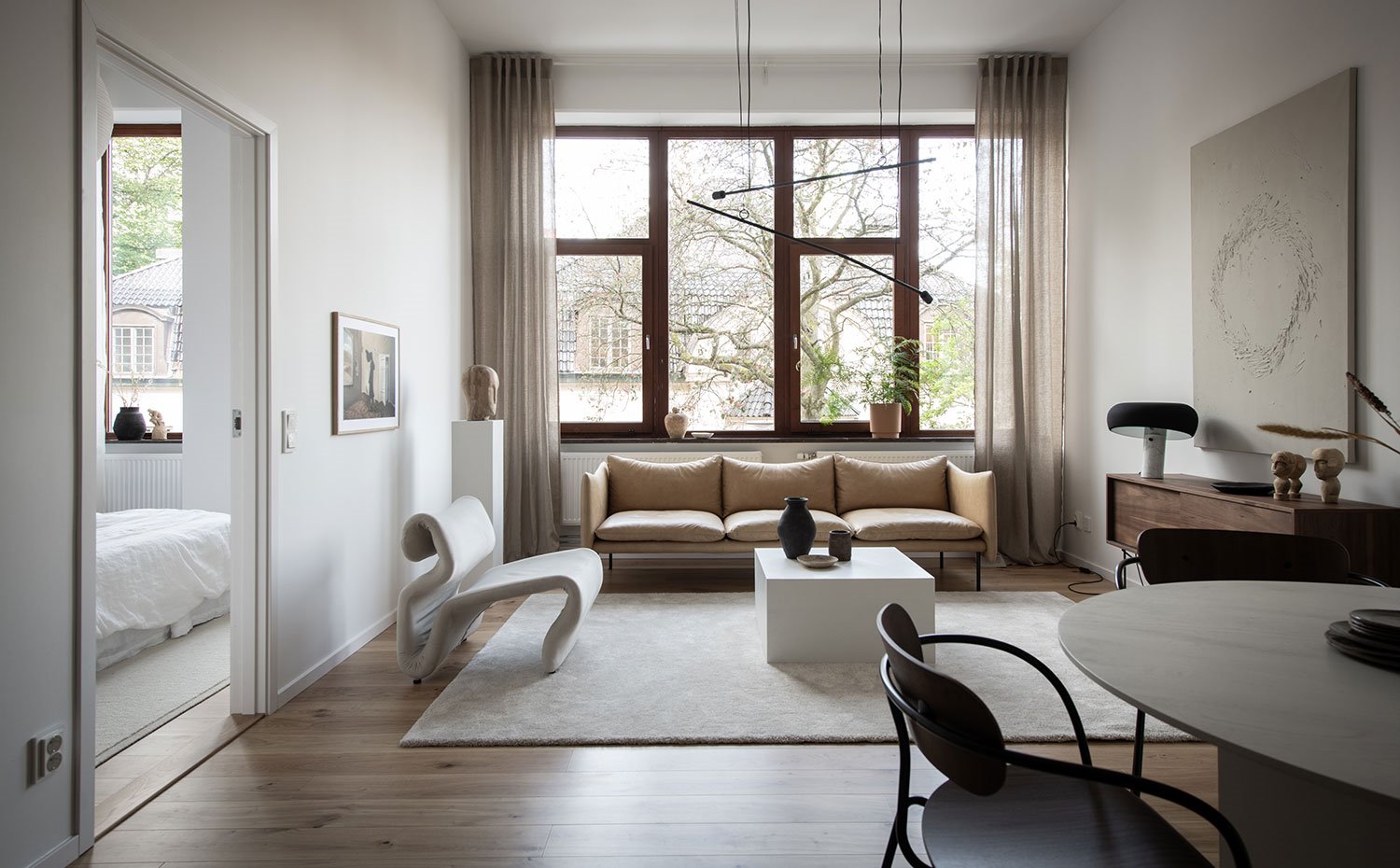 Salón con sobá y butaca, alfombra cruda sobre pavimento de madera, cortinas beige