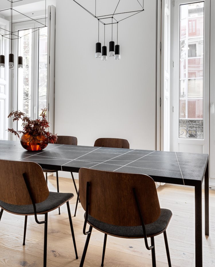 Comedor con luminarias suspendidas livianas en negro sobre mesa de comedor negra a rayas blancas, jarrón marrón, suelo de madera