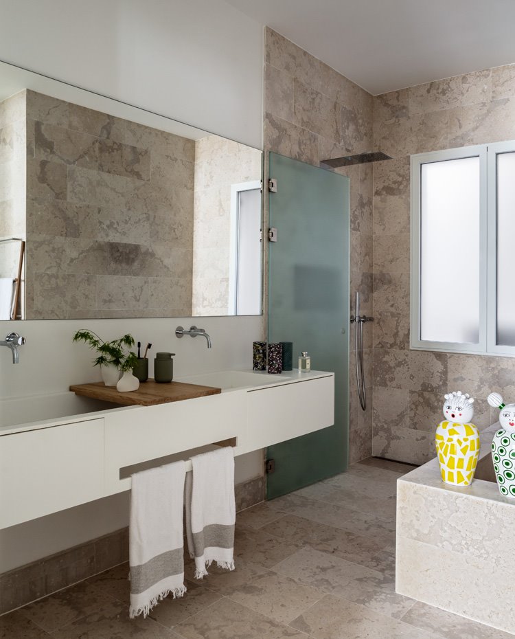 Revestimiento de piedra en tonos cremas, encimera de doble seno en blanco, puertas divisorias en cristal