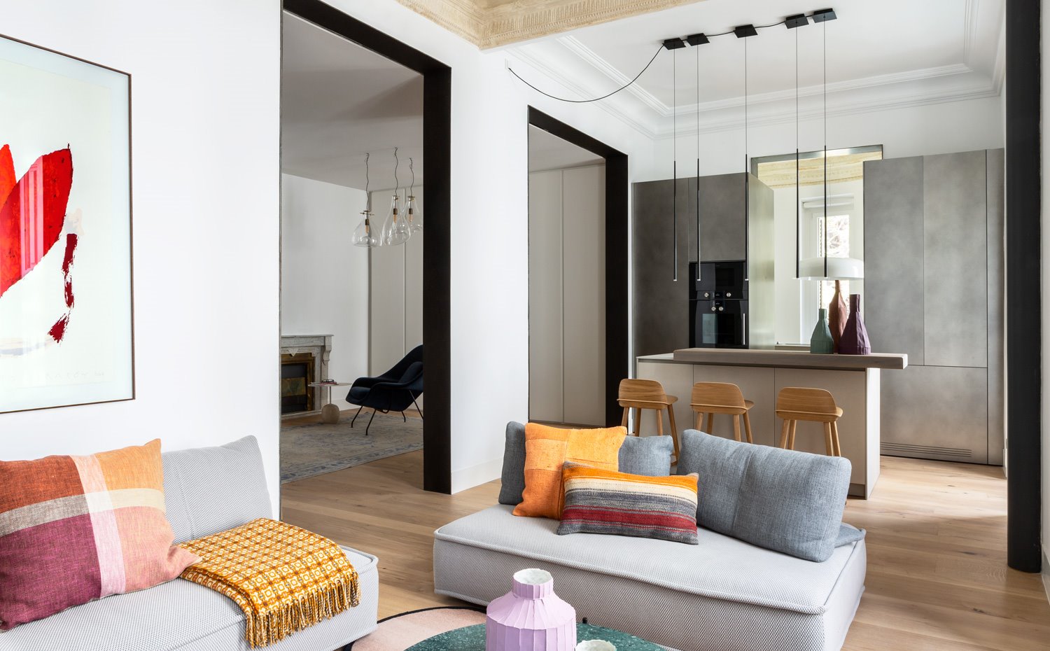 Salón con sofás grises y cocines amarillos y naranjas, aperturas en pared hacia rincón de lectura frente a chimenea