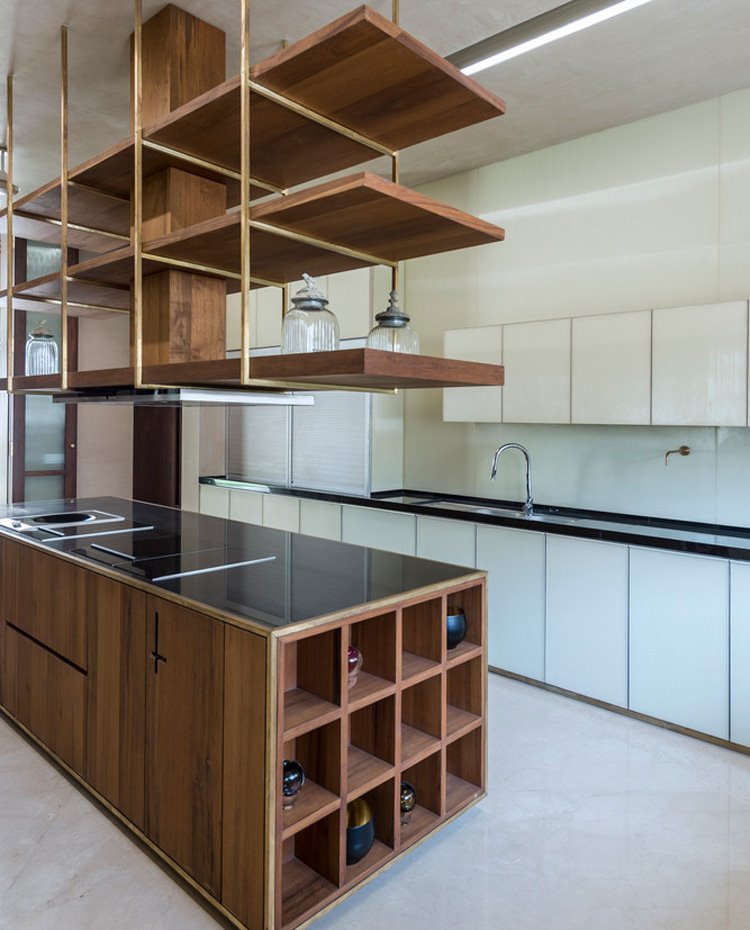Cocina con mobiliario de pared en blanco e isla central y estantes junto a campana en madera, encimera oscura