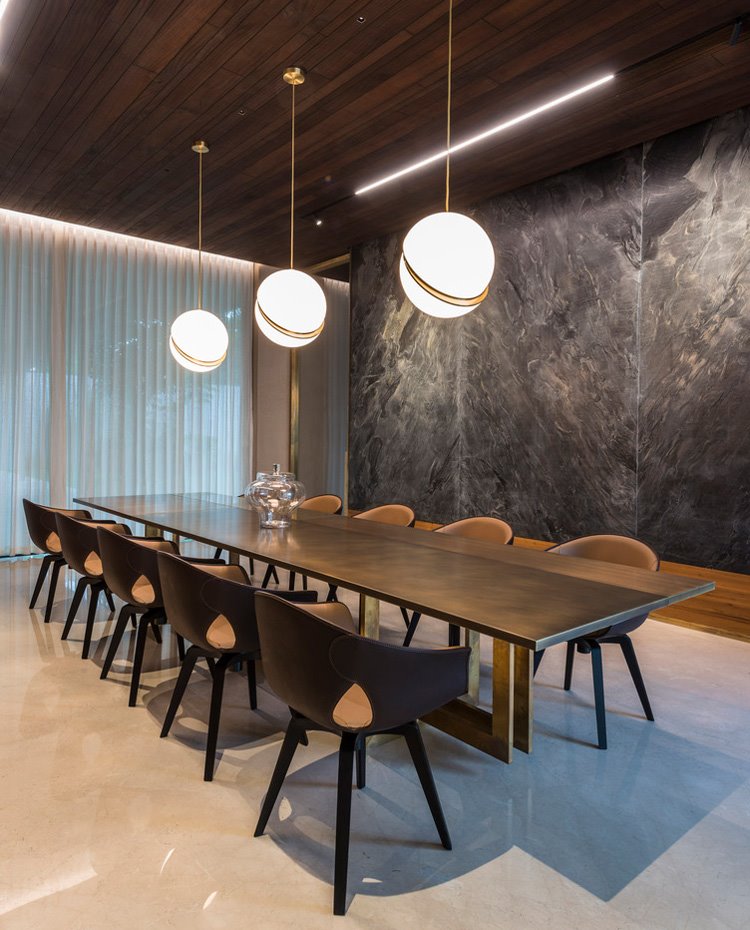 Comedor con larga mesa de madera y acabado cromado, sillas de madera y tres luminarias con pantallas redondas
