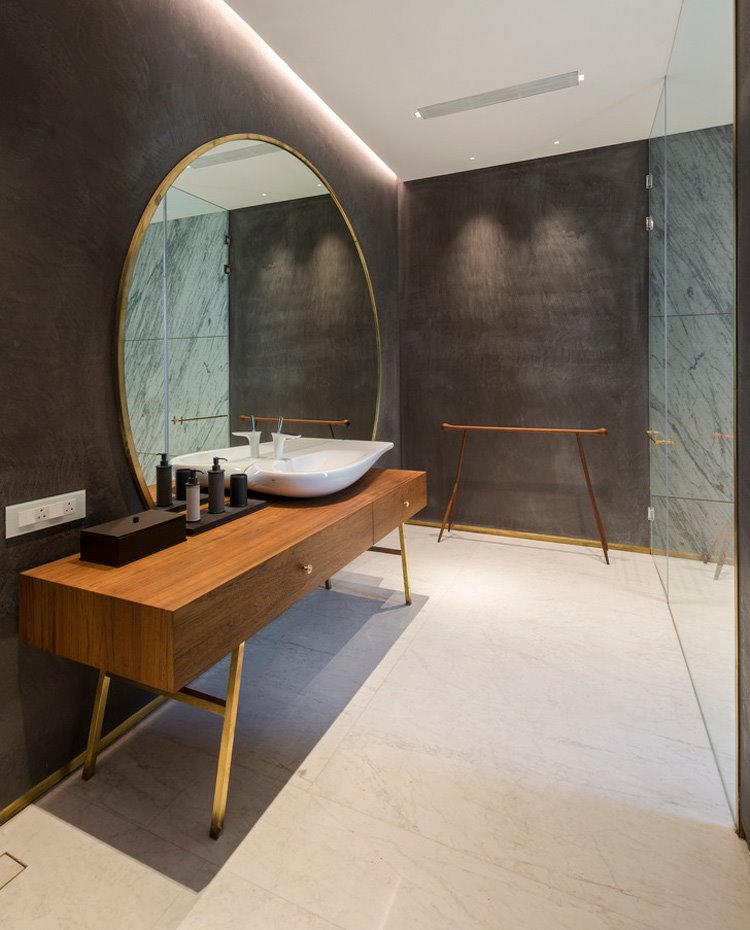 Cuarto de baño con espejo circular en zona tocador, mueble de madera y patas cromadas