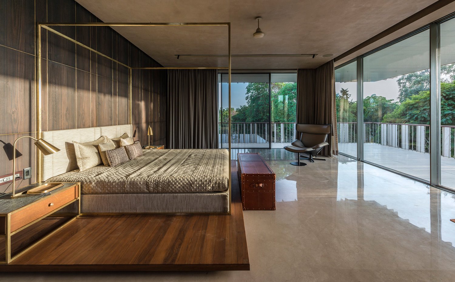 Dormitorio con cama sobre base de madera, estructura dorada y revestimiento de pared de madera, cerramientos acristalados