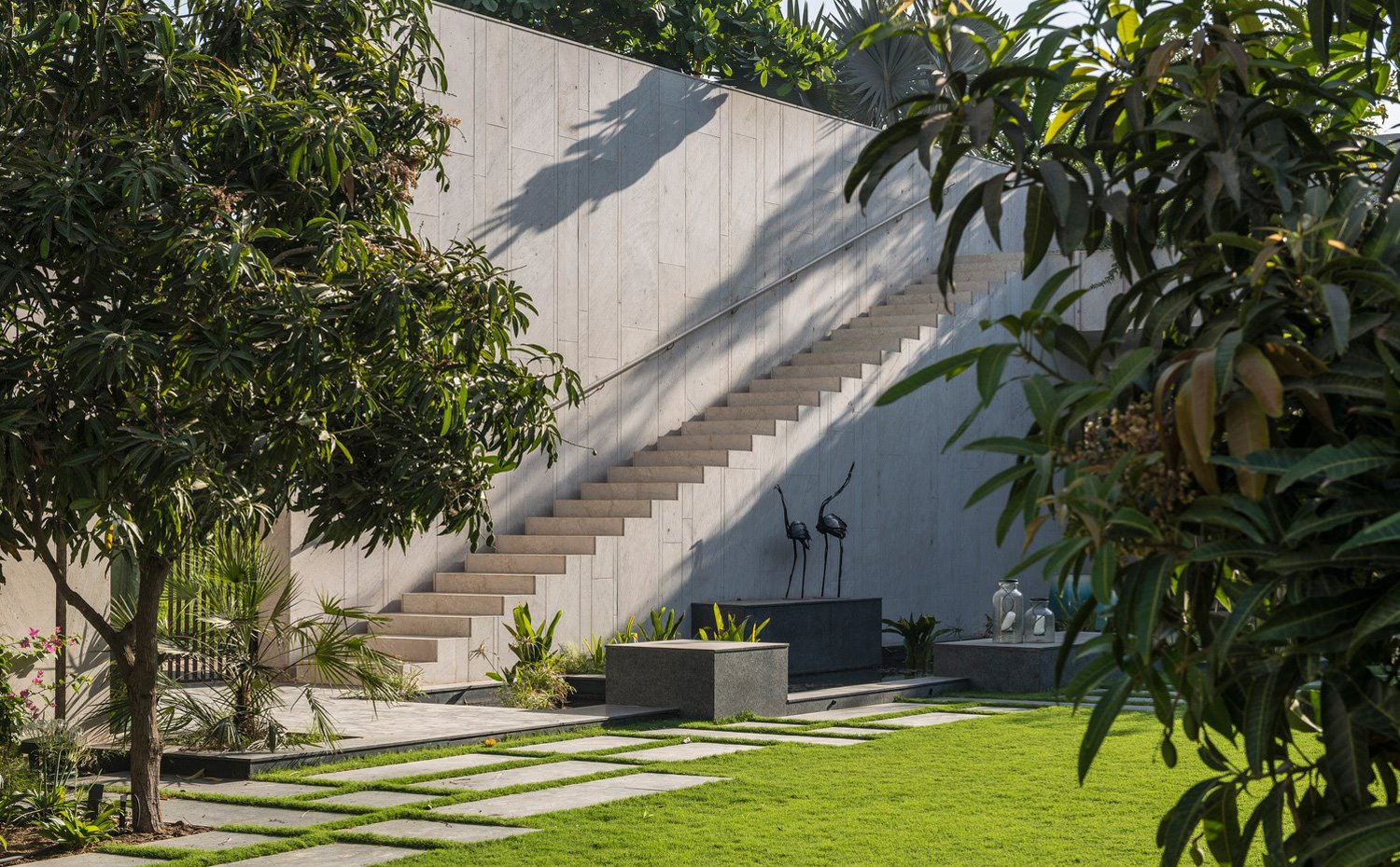 Exterior ajardinado, con estanque y esculturas de bronce y escaleras que comunican ambos niveles