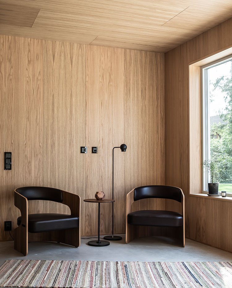 Butacas de madera y piel negra, mesita auxiliar circular, luminaria de pie en negro, revestimiento de madera