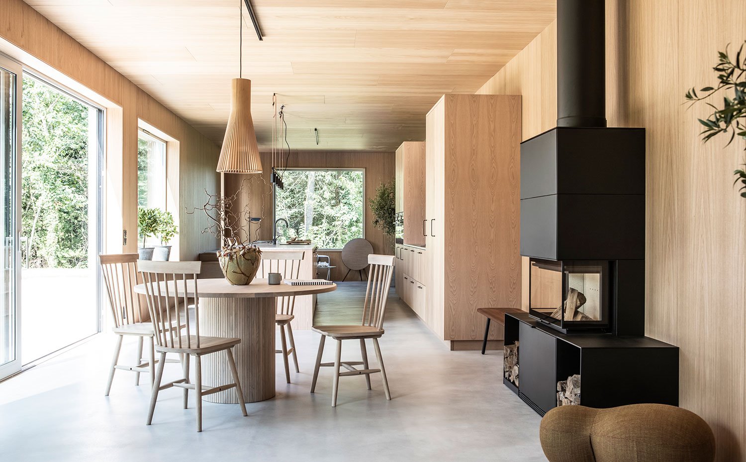 Comedor con chimenea y pouf marrón de formas ergonómicas, con la cocina y el salón al fondo
