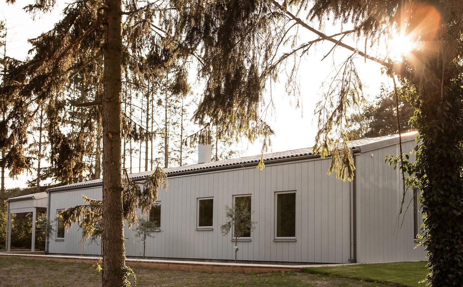 Exterior de la vivienda con fachada en blanco prefabricada, rodeada de árboles