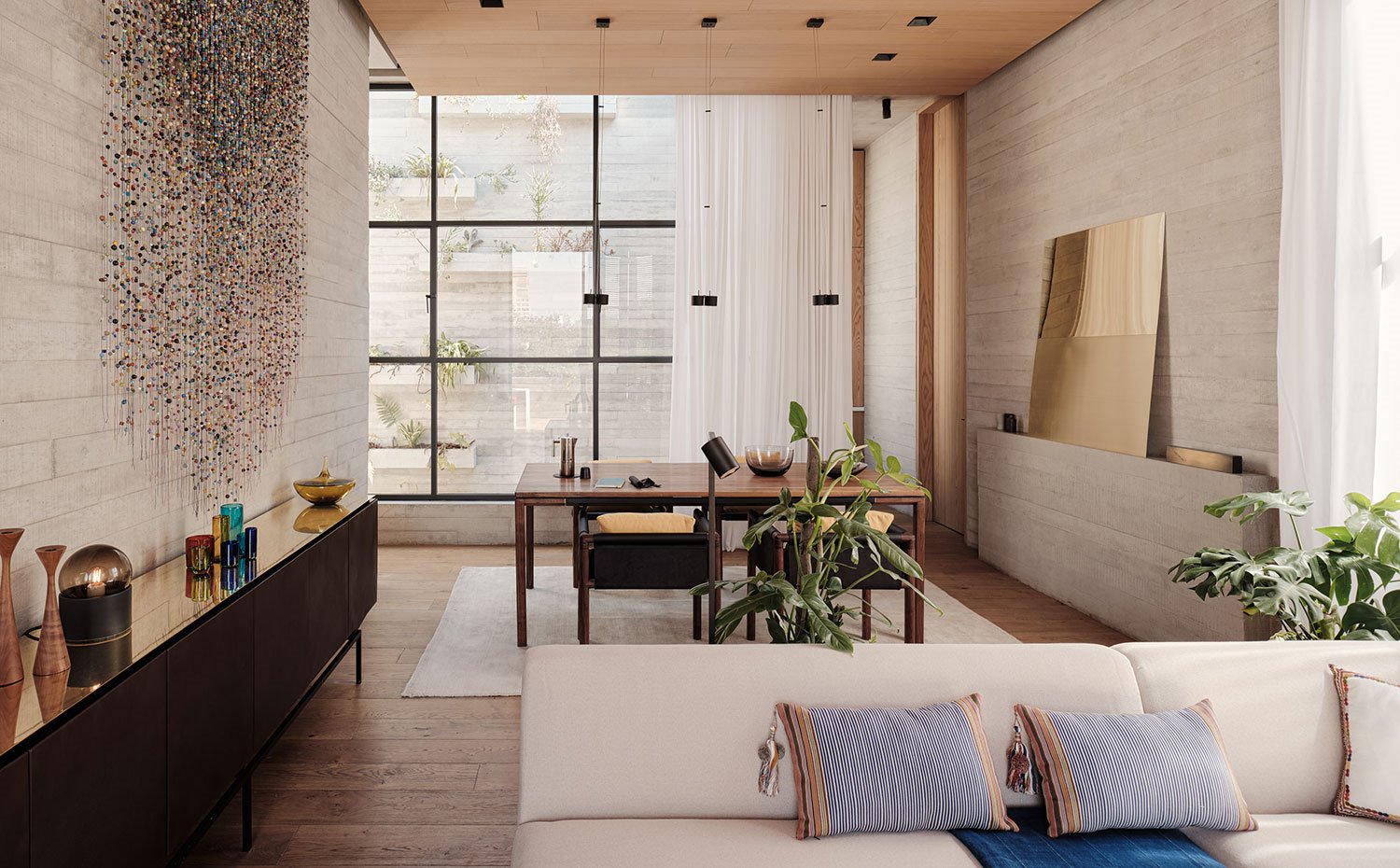 Comedor y con mesa y sillas de madera, afombra cruda y mueble contenedor revestido a juego de la pared, sofá en crudo y mueble bajo de madera