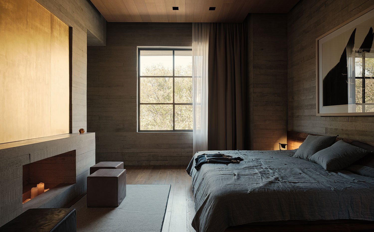 Dormitorio con chimenea bajo motivo decorativo dorado, paredes de hormigón, poufs marrones