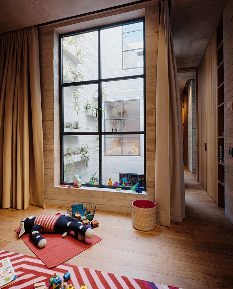 Habitación infantil con altos techos, gran apertura a patio interior, cortinas marrones, suelo de madera, alfombras en rojo