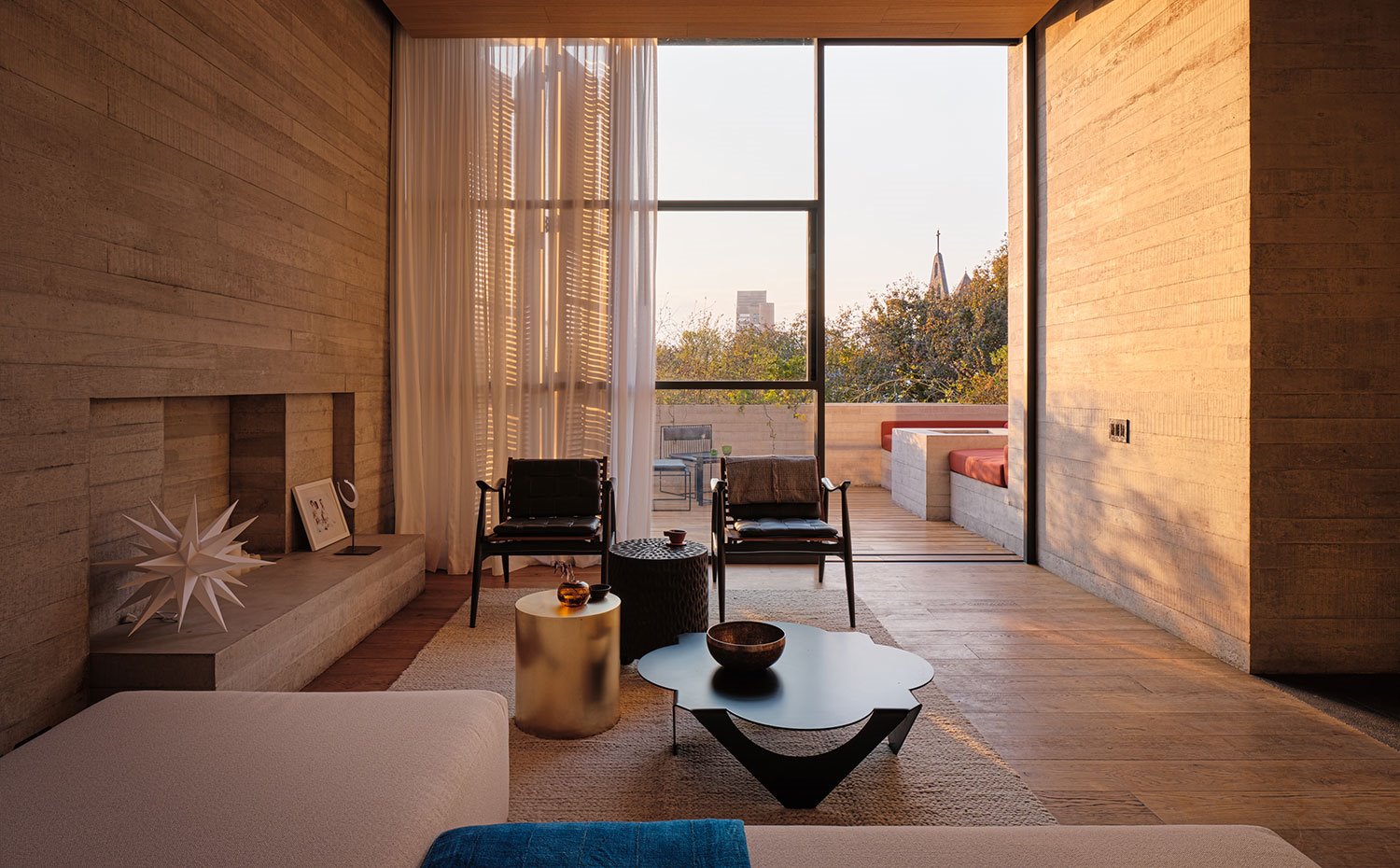 Salón interior con suelo de madera, butacas de madra y piel, sofá en crudo, varias mesitas de centro