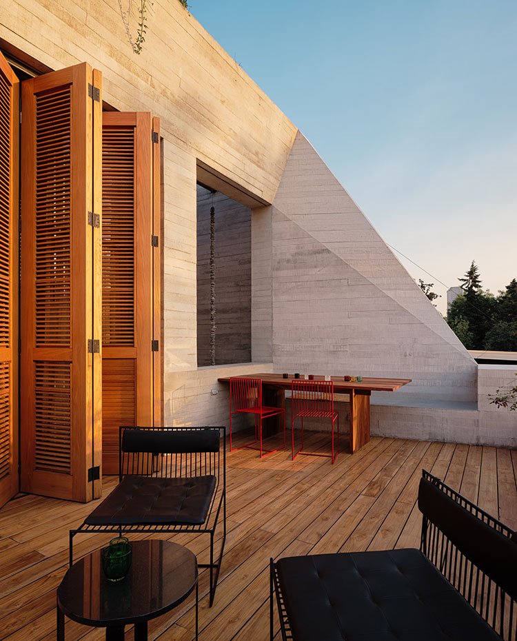 Terraza con sillas de rejilla y cojines en negro, mesa de comedor con sillas en rojo y paravientos con listones de madera