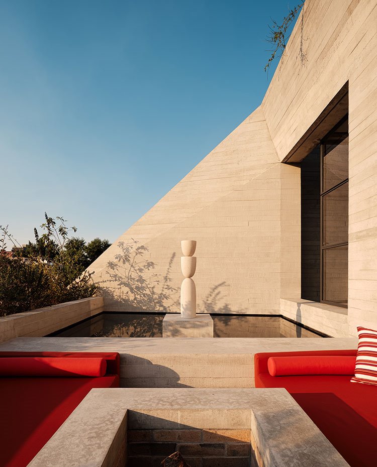 Terraza exterior con escultura acotada por agua, asientos en rojo con ocijines a rayas