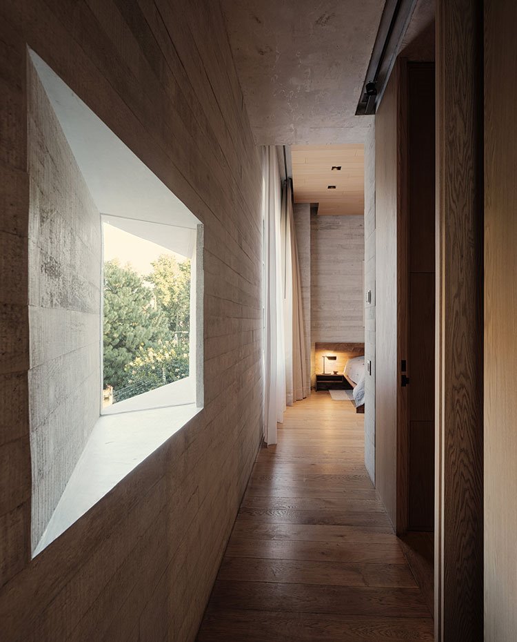 Zona de paso con pared de hormigón y apertura en ángulo, puerta corredera de madera hacia dormitorio