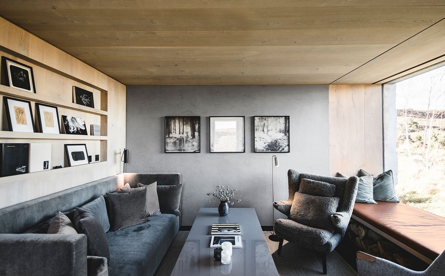 Sofá azul oscuro, butacas grises, mesa de centro gris, estantes de madera