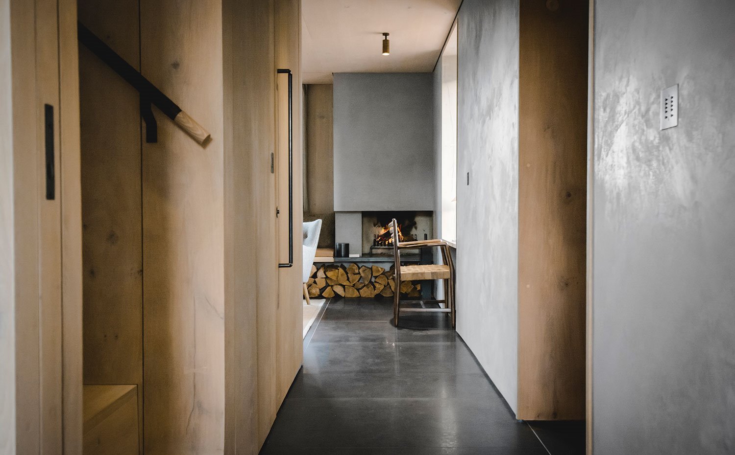 Zona de paso con chimenea de fondo con silla de madera, revestimiento de madera y estucado veneciano