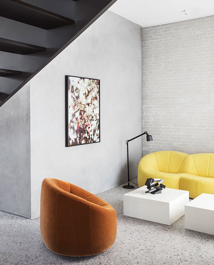 Butaca en naranja, sofá en amarillo, cuadro con motivos florales, luminaira negra y mesillas en blanco