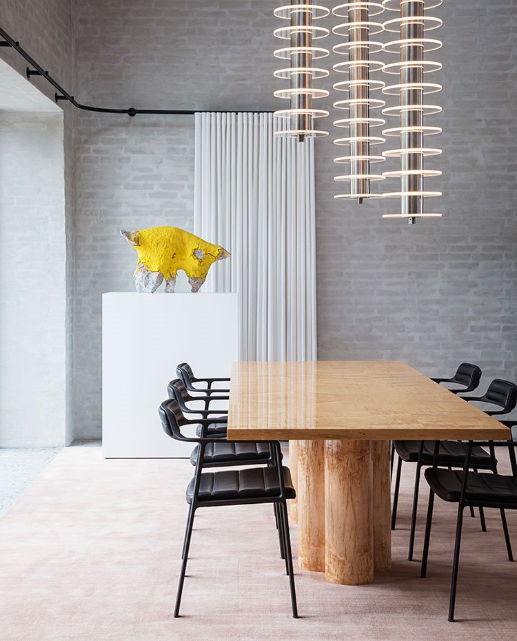 Comedor con mesa de madera, sillas en piel negras, luminarias futuristas, escultura en amarillo y cortinas sobre riel negro