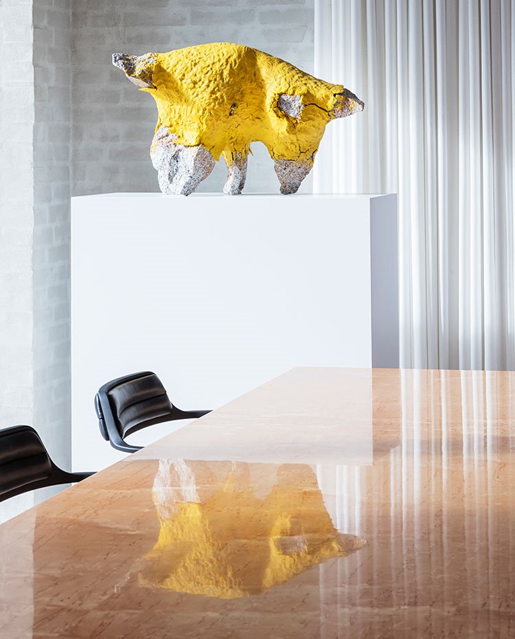 Detalle sobre mesa de comedor brillante en madera, sillas en negro, escutlra en amarillo