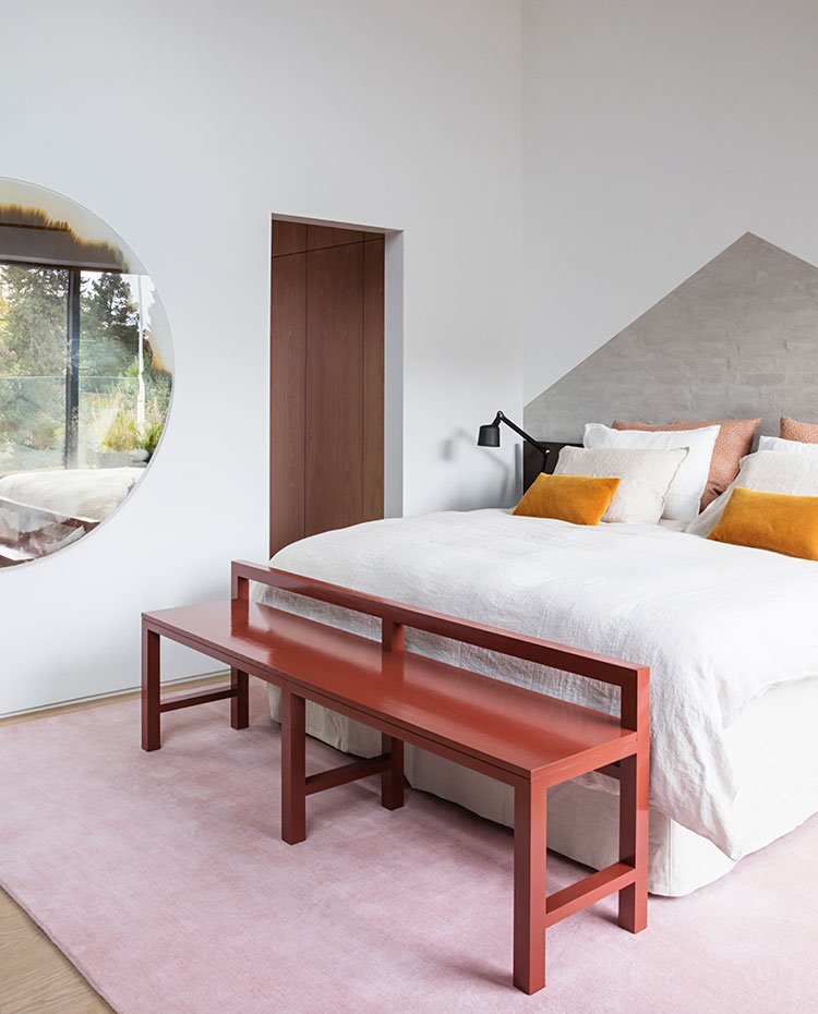Dormitorio con bancada en rojo teja, detalle cabecero de obra en hormigón, alfombra en rosa
