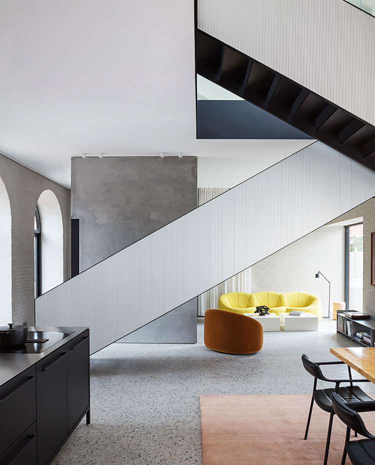 Vista de escalera como eje central de espacio, con la cocina y comedor en un lado y zona de estar al fondo