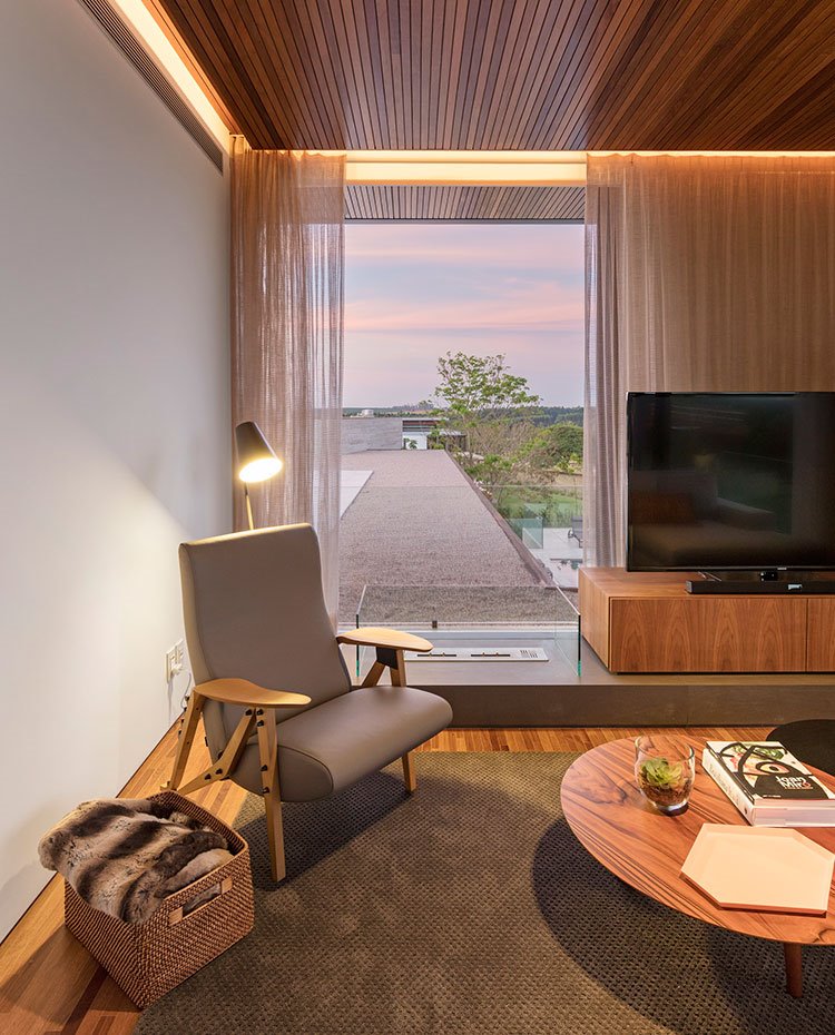 Rincon lectura con butaca gris, luminaria de pie, cesto para mantas, junto a mesa de centro y mueble de televisión