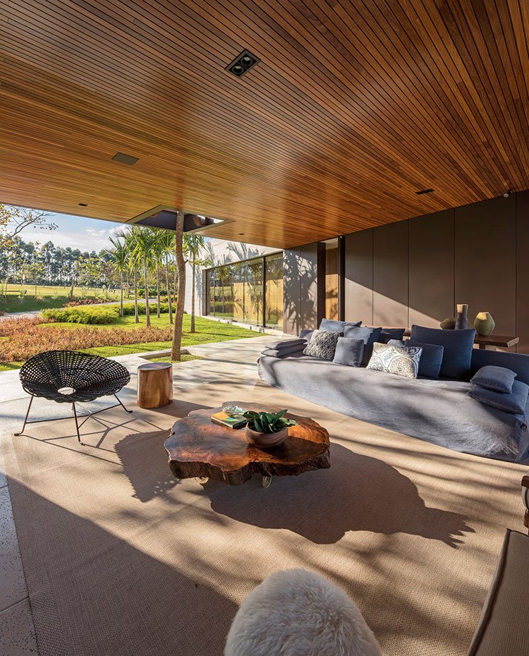 Salón exterior con alfombras de fibra natural, sofá en azul, butaca circular negra, mesa de centro de madera en forma de tronco