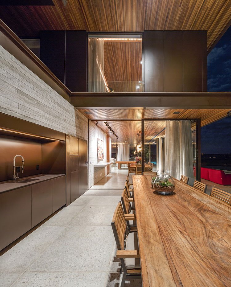Cocina-exterior-con-una-gran-mesa-de-madera-y-sillas-de-madera,-frente-de-cocina-en-marrón,-cerramiento-de-cristal-de-estructura