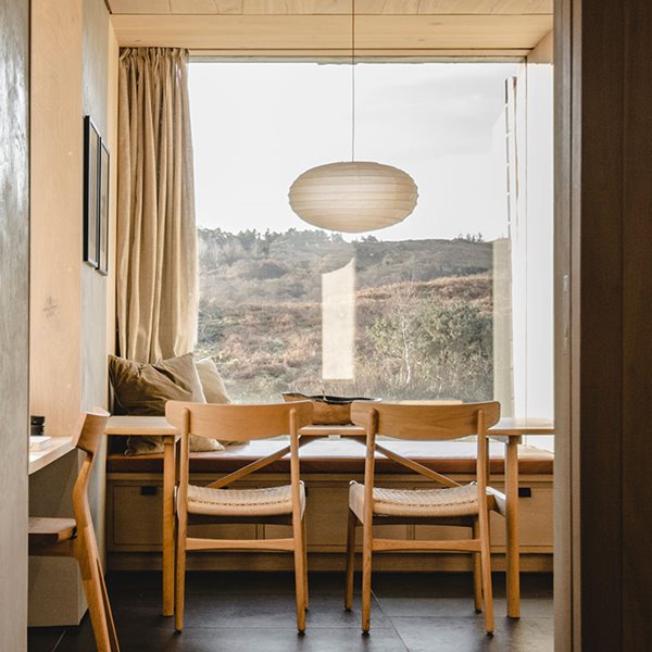 Zona comedor con sillas de madera, luminaria suspendida con pantalla ovalada, foco negro integrado en techo laminado en madera