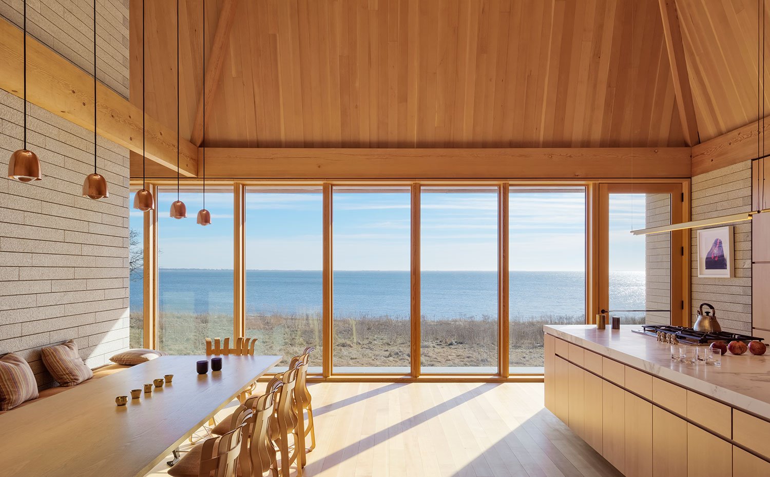 Mesa de comedor de gran longitud, en madera, banco corrido y sillas de madera y cojines en tonos neutros, isla de trabajo