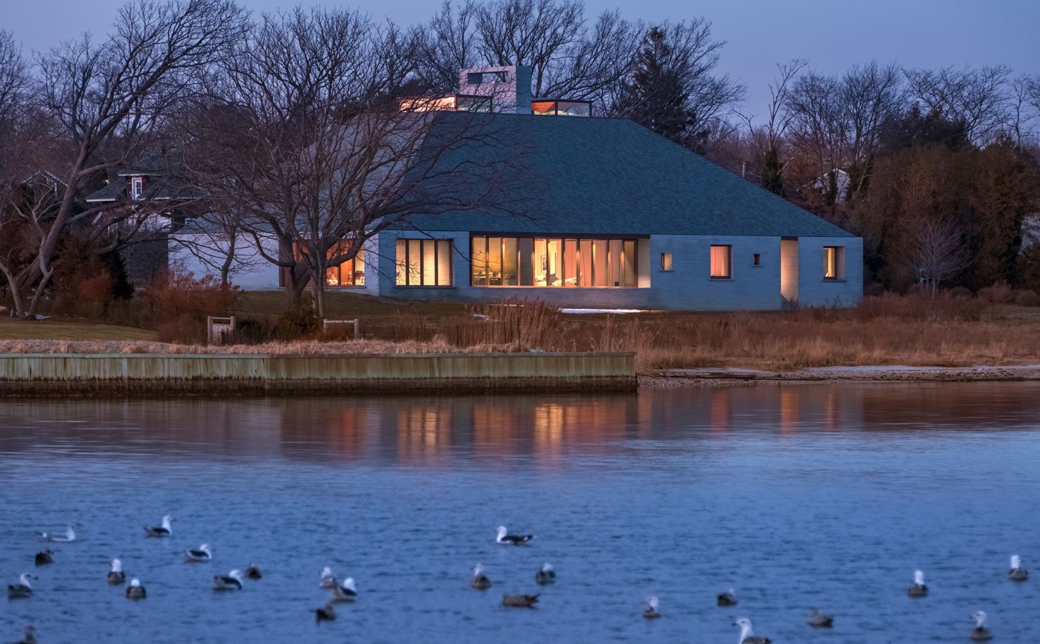 Vista al anochecer junto al lago con iluminación interior de vivienda abierta