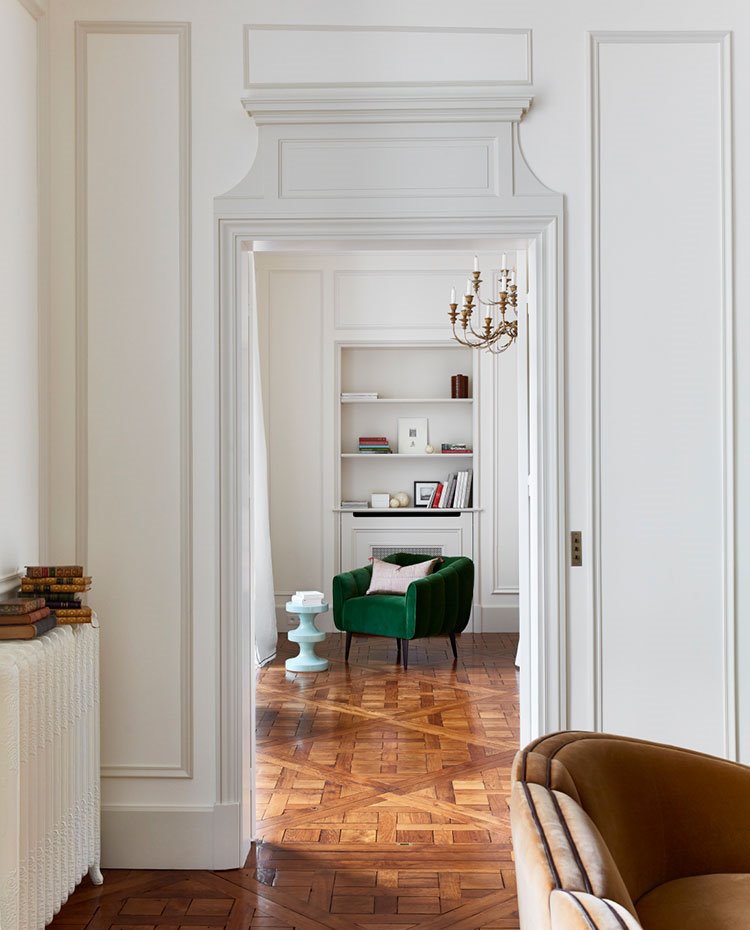 Butaca verde de fondo, librería en pared, pareds y puertas con molduras y detalles en gris, sofá en crudo