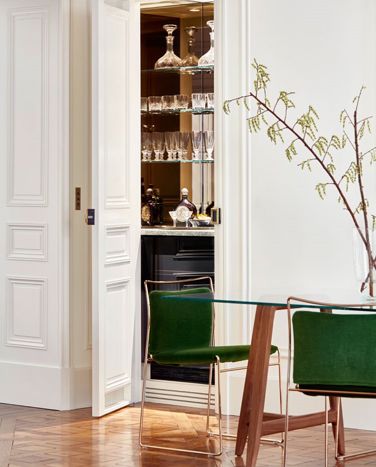 Comedor con sillas en verde, estructura dorada, mesa con patas de madera y sobre de cristal, armario minibar