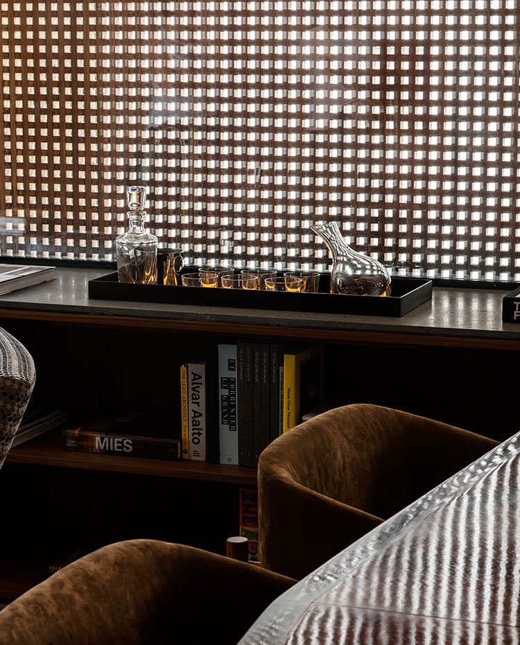 Detalle de asientos tapizados de terciopelo marrón, mueble bajo y bandeja con cristalería en tonos amarillos